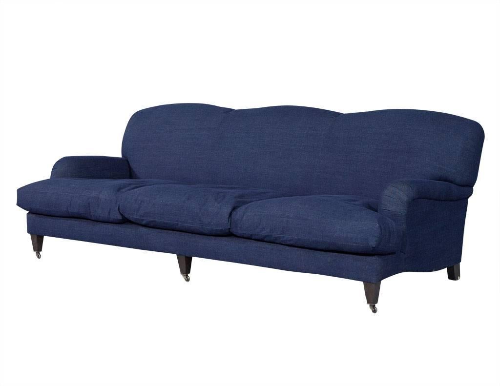 This comfortable, old world inspired Ralph Lauren sofa with English arms is wrapped in durable, denim upholstery. It sits atop tapered legs with casters to give it a modern Industrial feel. Comes with three plush down and feather cushions in two