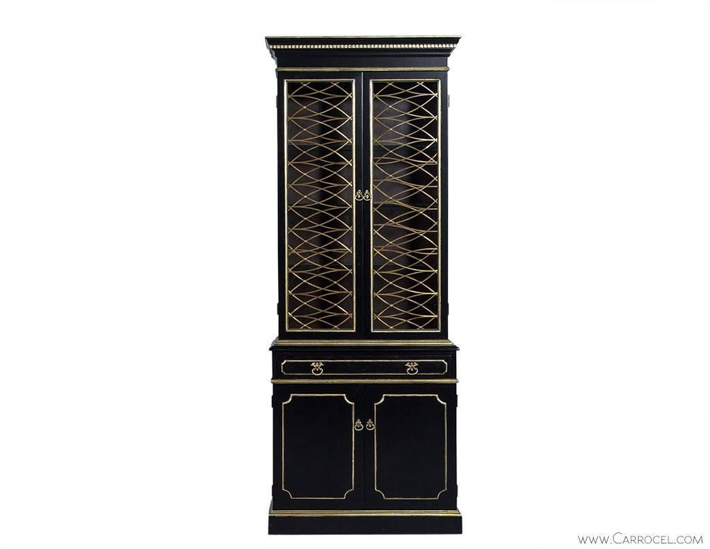 Stunning display cabinet features a custom Obsidian hand-rubbed black finish with gold leafed detailing. The top compartment is for display with two glass doors laced up in fine brass. The lower compartment has a drawer over a larger shelved storage