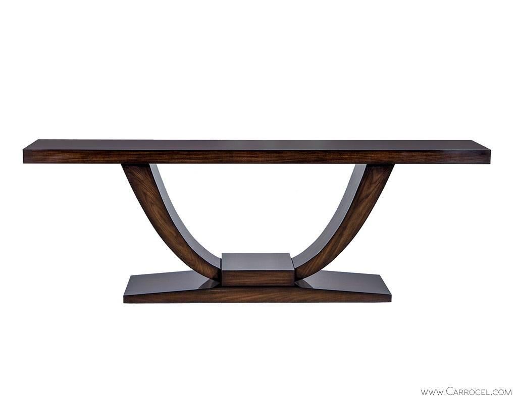 This walnut console table is crafted to order. Crafted in a deco style the tapered plinth base rests on the floor with the U-shaped extensions forming supports. This console table may not take up much space, but it will add a sophisticated air and