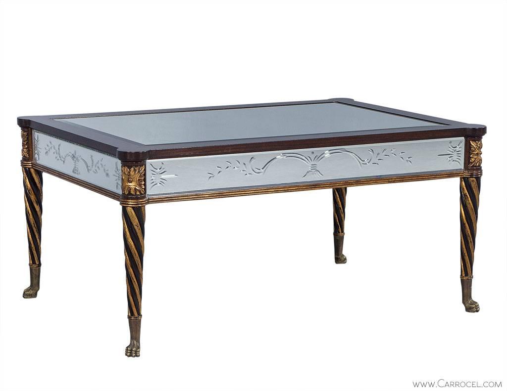Crafted in a traditional style, this mirrored cocktail table by EJ Victor has been constructed out of mahogany with giltwood accents along the twisted legs and floral motifs. With the legs terminating in brass paw foot caps and the top inset with