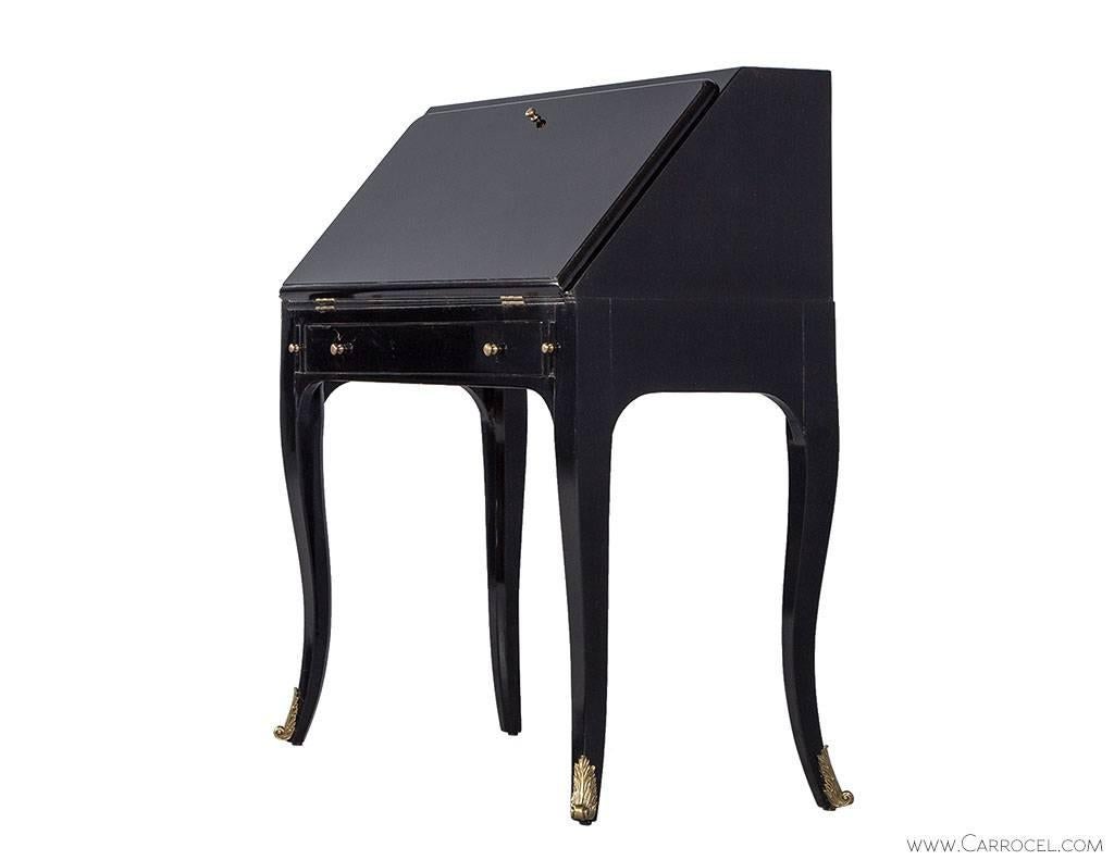This is a stunning 18th century inspired lacquered black bureau with long thin cabriole legs and decorative brass mounts. The slanted front door opens up to reveal a compartmentalized interior along with a leather writing surface. Great for a