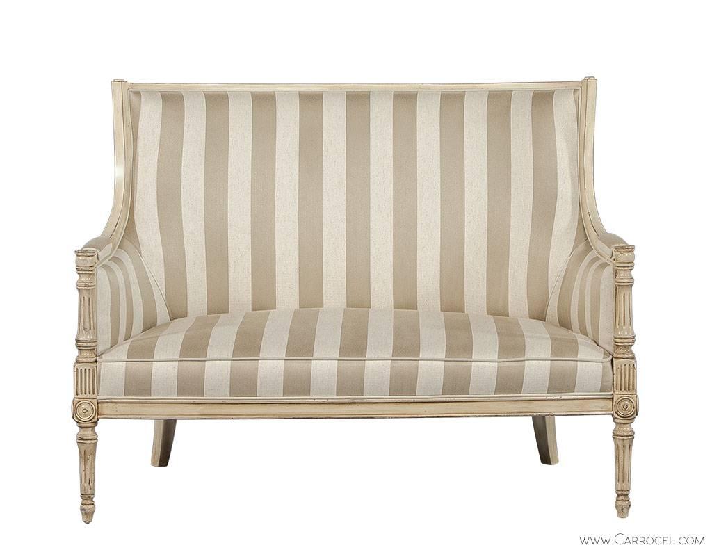 This settee was made in a classical Louis XVI style using natural and neutral toned striped upholstery and a distressed French cream finished frame. The framework has been carved out of beechwood with an intricate and flawless finesse. Made in Italy