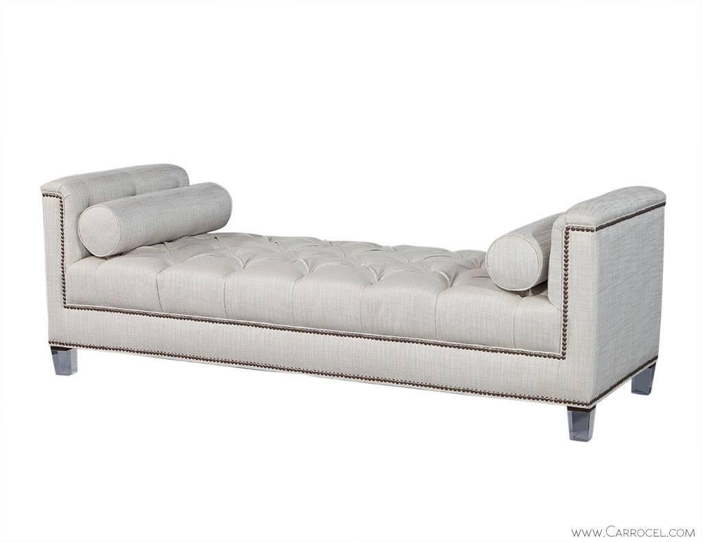 This custom daybed is wrapped in light beige woven fabric and adorned with brass head-to-head nail trim. It sits atop tapered lucite legs, has a luxurious diamond tufted top and comes with two roll pillows to not only add to the elegance but also to