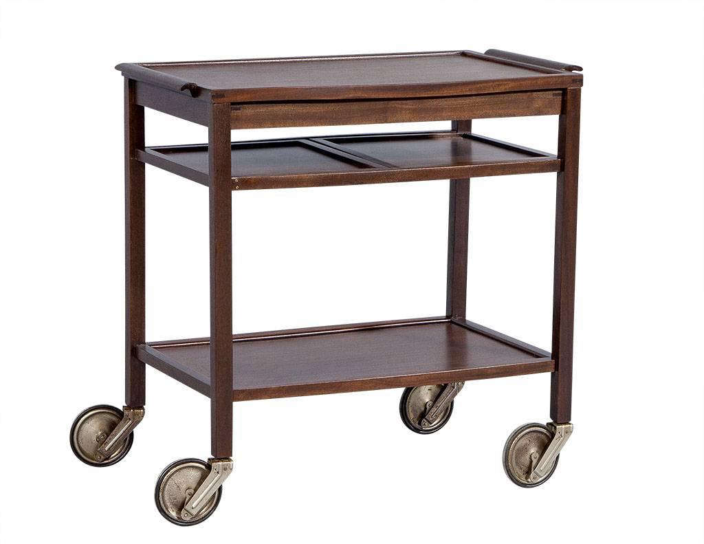For the minimalist entertainer, this Mid-Century Modern bar cart is made of durable teak wood and finished in a smooth cognac. There is a pull-out shelf for extra storage and the lower shelf is the perfect place to store bottles and other serving