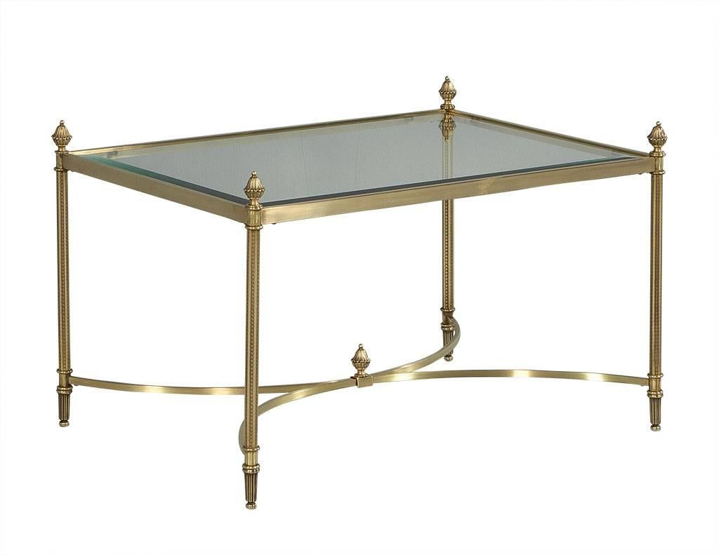 This Classic Maison Jansen cocktail table boasts a brass frame and fluted legs with decorative finials on top. Below stretchers reach to the center meeting in two opposing curves adorned by another finial. The beveled edge glass tops adds a touch of