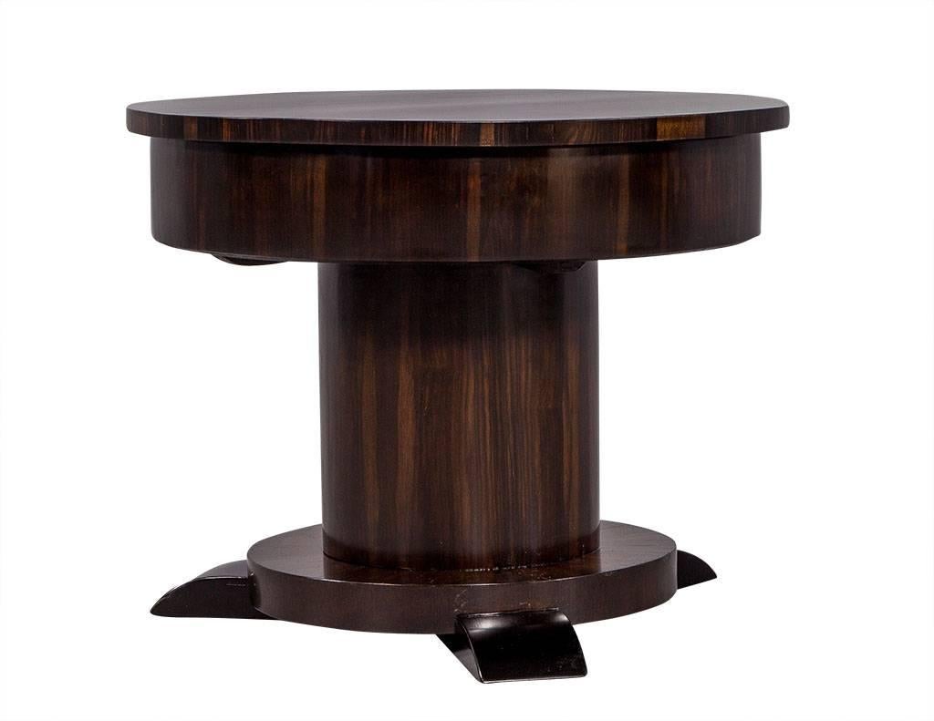 This bold Art Deco table is more than meets the eye. The outside is crafted out of French Macassar ebony with a rich, dark finish and lighter striation from the wood grain. It rests atop a central column pedestal and three black feet, and once the