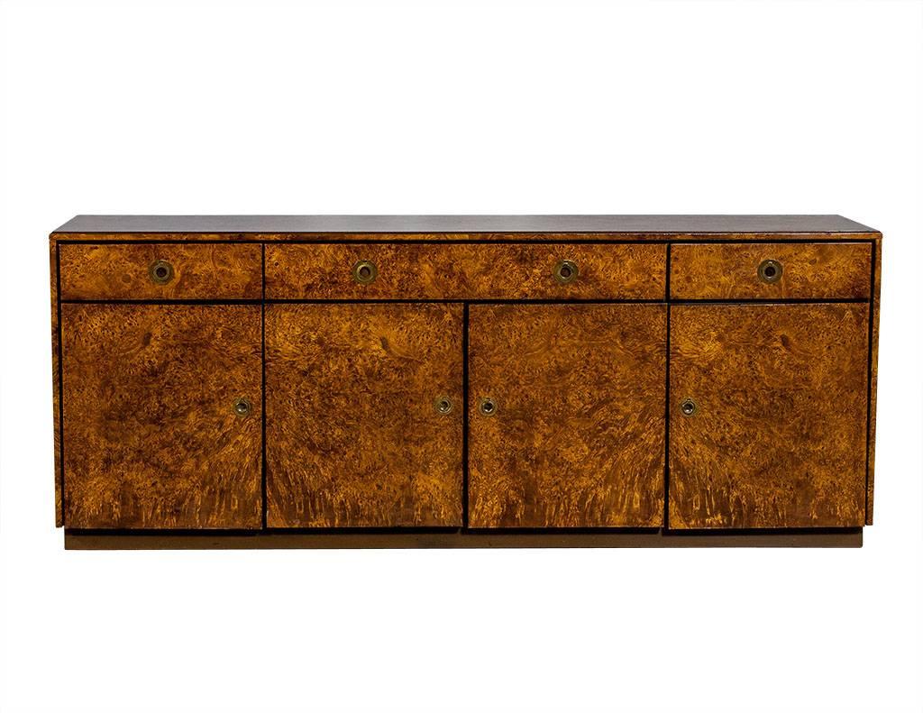 This gorgeous buffet is Mid-Century Modern in style and made of rich, burled wood. It has a total of three drawers with fabric lining in the middle double drawer and inserts for cutlery and stem wear. The four lower compartments conceal shelves and