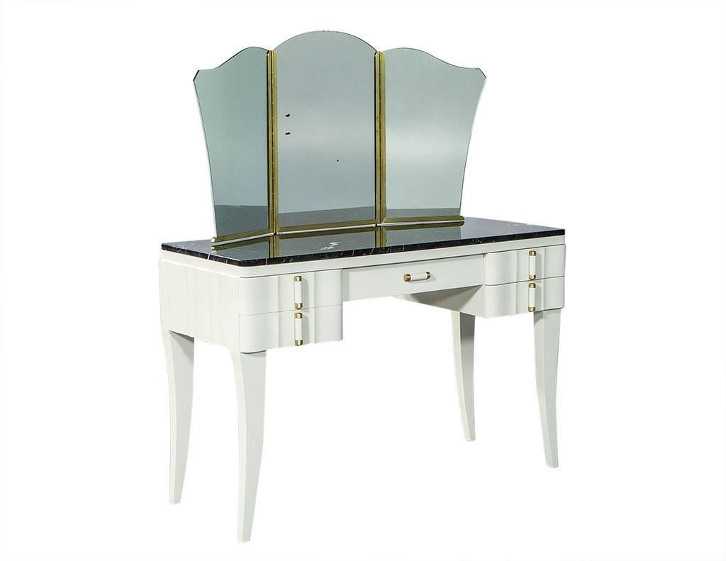 This newly restored, French-style Art Deco vanity has a light grey high gloss wood case with matching drawer handles accented with brushed brass. It sits atop saber legs, has five washable fabric-lined drawers and has a scalloped edge tri-fold