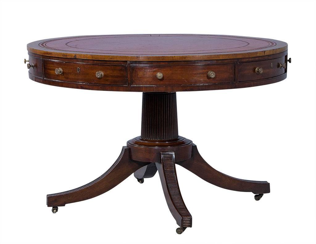 Classic, circular rent table with an inlaid red leather top and gold tooling. Sits atop a reeded pedestal with four legs on casters for mobility. All original brass hardware and four green felt-lined drawers. Perfect for game night!