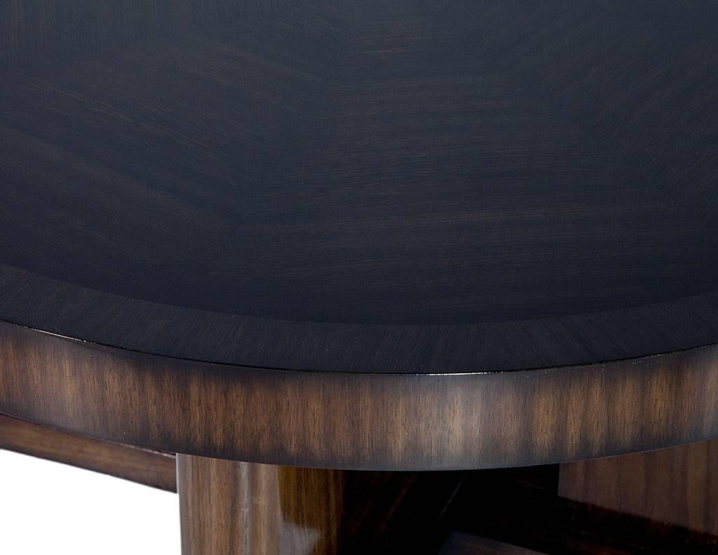 This modern, round cocktail table is crafted out of Macassar ebony and coated in a high gloss espresso finish. It sits atop a four leg X-shaped pedestal and is a great centerpiece for a bold living space.