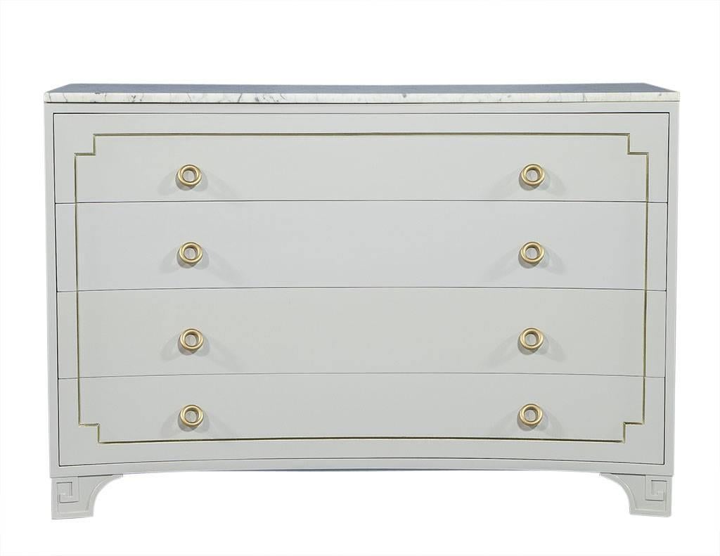 This neoclassical chest is made of mahogany with a concave façade and inset brass trim. Boasting marble top with light grey veining and gold circular brass pulls. There is a greek key motif on the legs and finished in high gloss light grey lacquer.