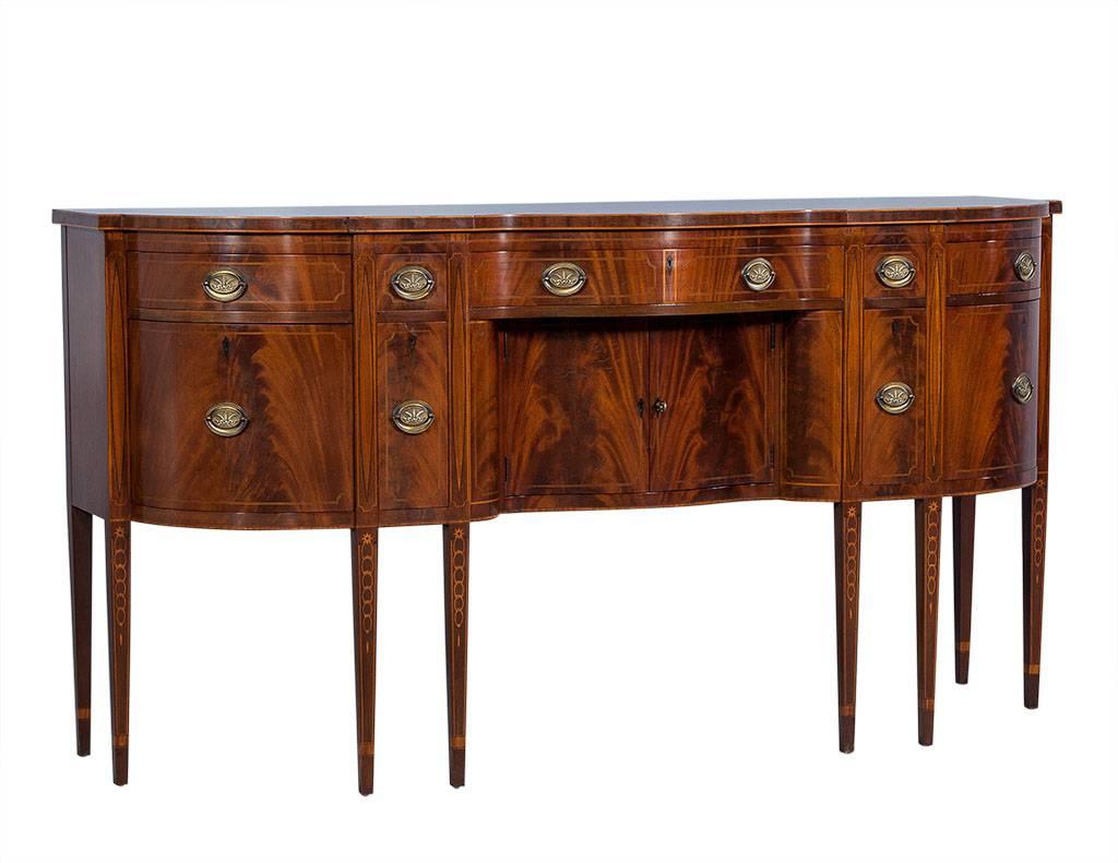 This intricate, American Federal style sideboard is crafted out of flamed mahogany and houses seven drawers along with two lower cabinets with one key. The marquetry motif down the legs is by Williams-Kemp and the case is serpentine in shape.