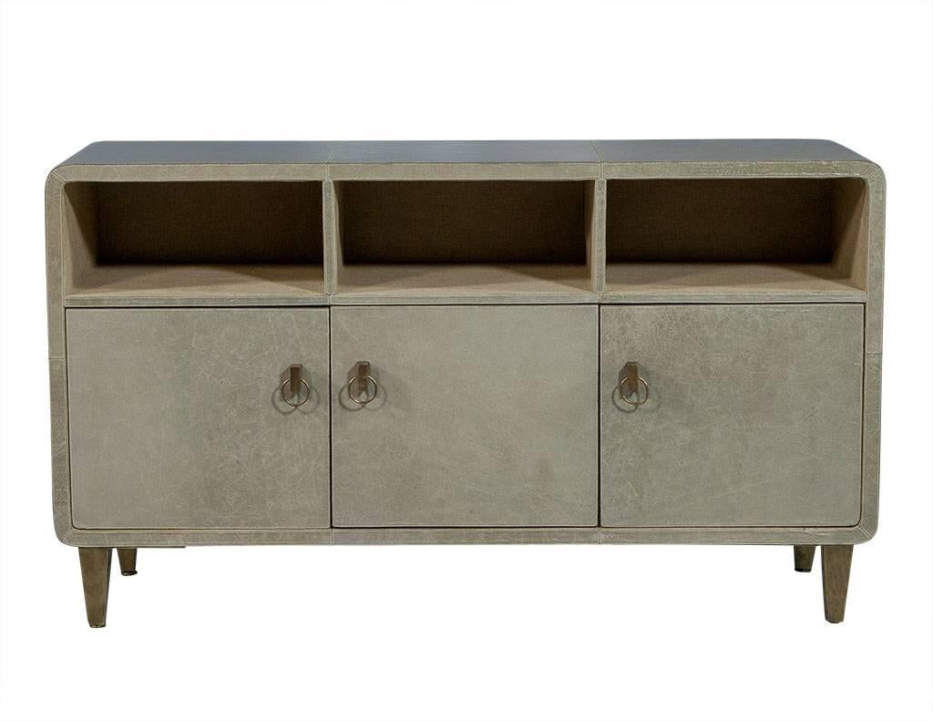 This Mid-Century Modern sideboard is beautiful yet subtle. Wrapped in pale sage distressed leather with white stitching, it houses three upper display shelves and three lower cabinets. The entire interior is lined with textured linen and has antique