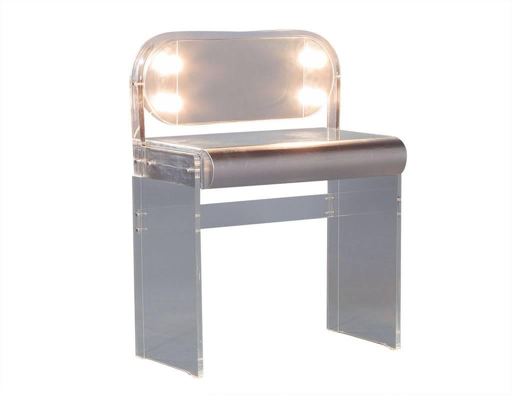 This stunning Mid-Century Modern vanity is perfect for the movie star in your household. The frame is crafted out of Lucite in a waterfall design with a mirrored glass top adorned with four makeup lights for true star power. The final touch is a