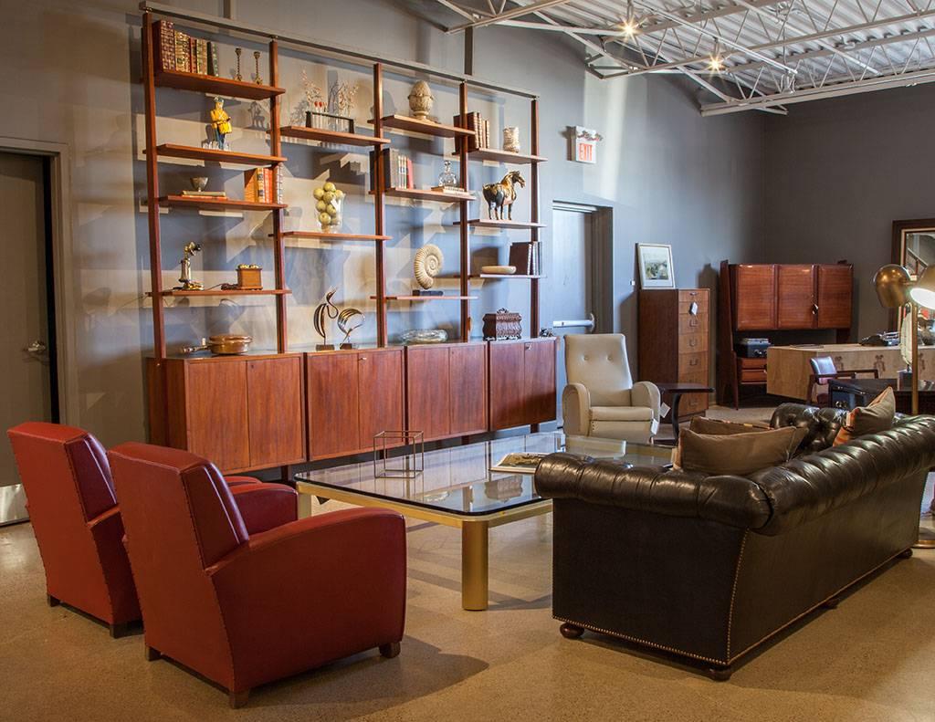 This Mid-Century Modern wall unit straight from Denmark has a very trendy, Industrial feel. Crafted out of teakwood, it showcases 18 shelves and lower cabinets with interior shelving for storage that open with a brass lock and key. The top is gold