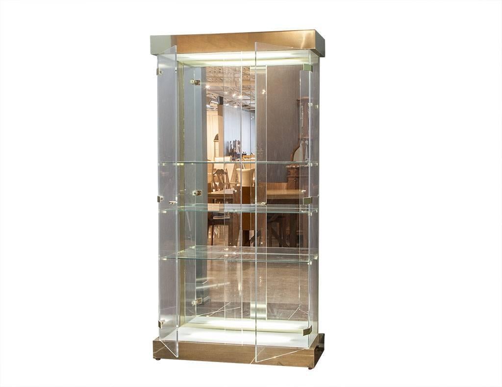 This beautiful Mid-Century Modern curio cabinet is comprised of a brushed brass accented display vitrine with Lucite doors. Inside are three glass shelves with illumination at the top and bottom and a mirrored glass inside back. A perfect addition