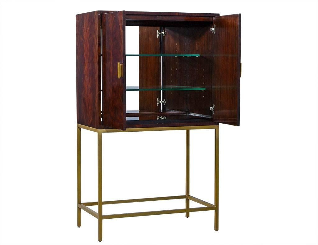 This contemporary bar cabinet is made of flamed mahogany in a deep cherry finish. It sits atop a slim, four leg brass base with matching pull handles and a mirrored back interior with two glass shelves. A funky piece perfect for entertaining.