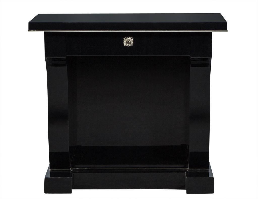 This neoclassical style nightstand is a truly striking piece. It has a single drawer with a laurel wreath escutcheon and an overhanging harp-shaped pedestal sitting atop a plinth base. A perfect fit for a bold bedroom.