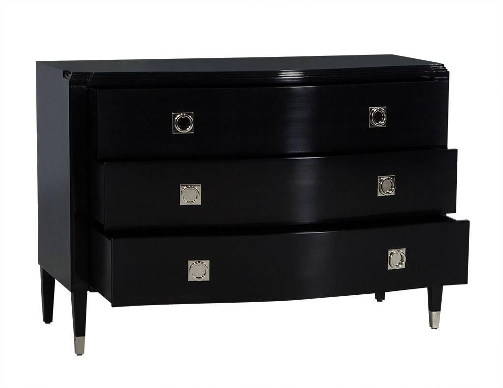 This transitional style dresser has three drawers and is finished in a rich, black lacquer. It features a serpentine top and bit of glitz with stainless steel ferrule pulls. The piece sits atop four fluted legs with stainless steel caps on the two