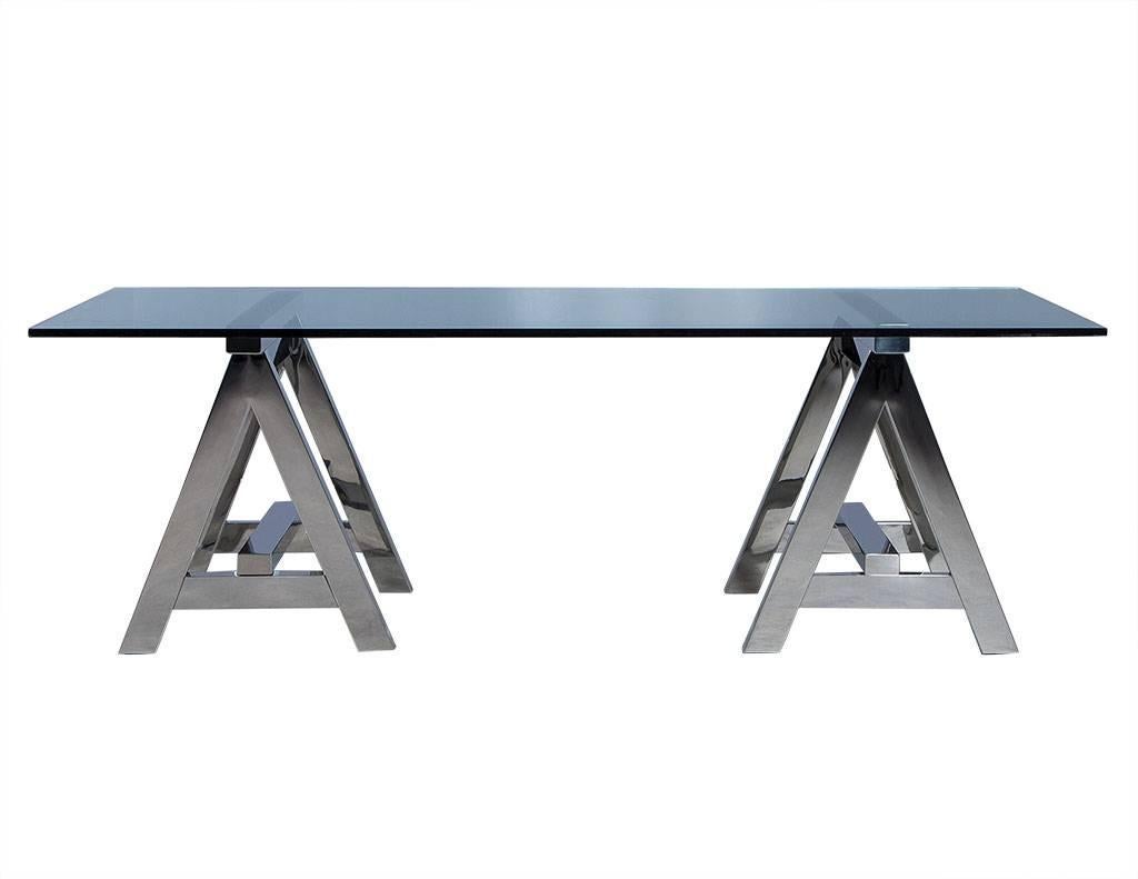 Contemporary dining table. It is comprised of a half-inch glass slab sitting atop two stainless steel sawhorse pedestals. A sleek and modern addition to any dining area.