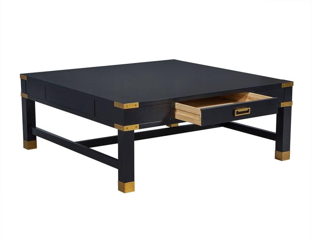 This Campaign style cocktail table is designed by Alexa Hampton. It is an elegant piece crafted out of square mahogany with two drawers and a lower shelf. It features brass corner straps, ferrules, pulls, and a middle stretcher that stands out