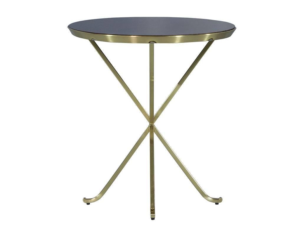 This transitional style side table was designed by Aerin Lauder. It is a trendy piece, with a round, inset mahogany top in a dark cherry stain atop a polished brass cross leg frame. Perfect for adding a bit of flair to a dreamy seating area.