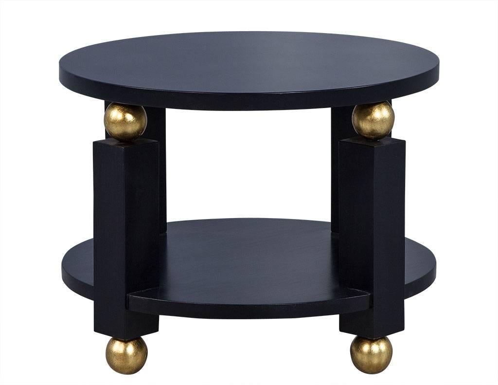 This French Art Deco round end table features two floating shelves and sits upon four square columns, supported by four gilded spheres on both bottom and top shelves. Finished in a matte black, it is sure to add a unique and dramatic flair to any