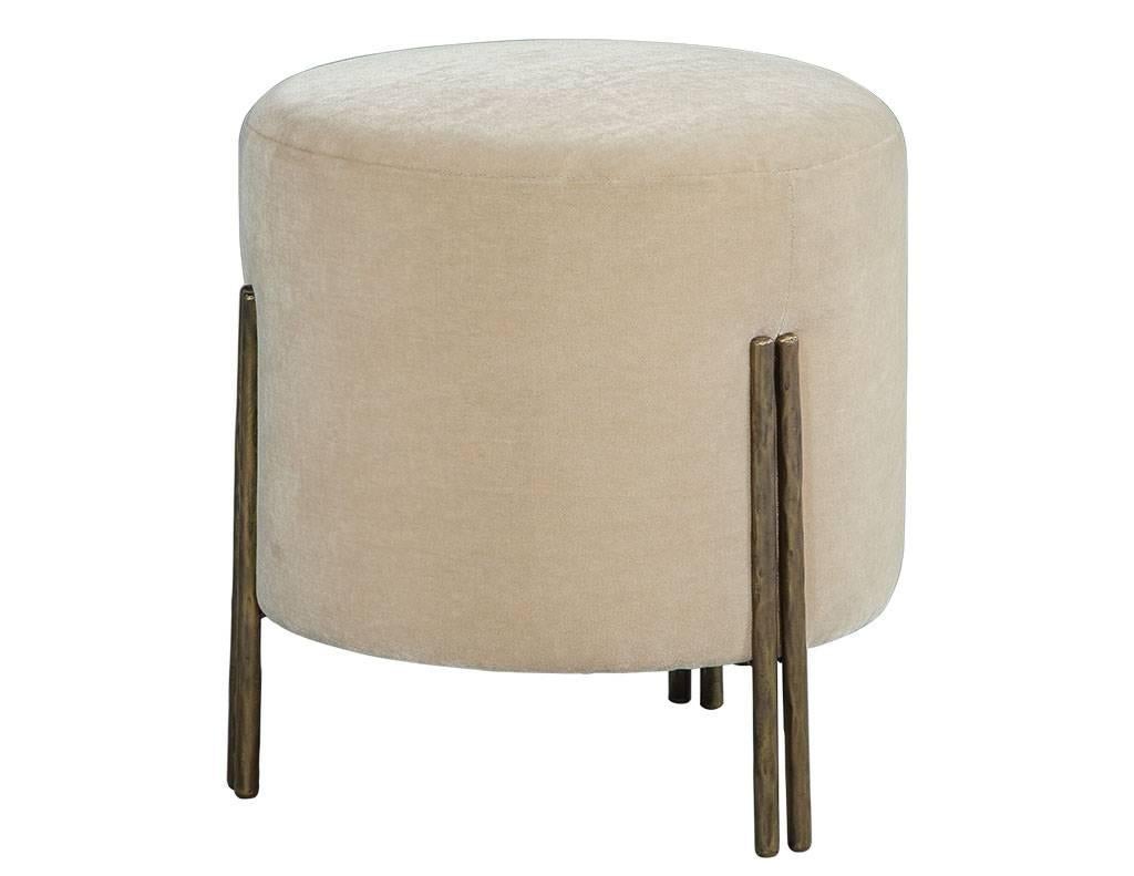 This modern foot stool is sleek and luxurious. It sits low, featuring brass legs in a textured, burnished bronze finish and a seat covered in ivory velvet fabric. A gorgeous piece to go with a neutral or even bright sofa set.