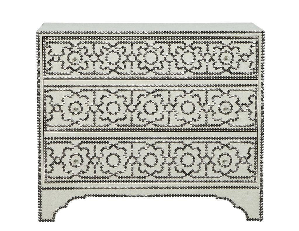 This transitional style chest is gorgeously designed. It is completely wrapped in off-white linen and decorated with nailhead trim. It contains three large drawers and sits atop a scalloped base on bracket feet. A uniquely chic addition to a