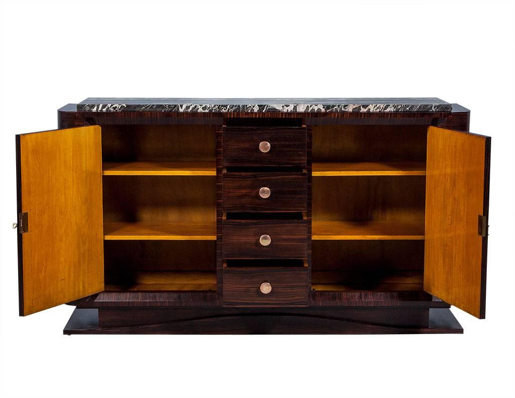 This Macassar ebony buffet is divided into three organizational compartments. Left and right side includes two shelves, while middle section includes four drawers. Accented with copper hardware and detail the piece includes an original black and