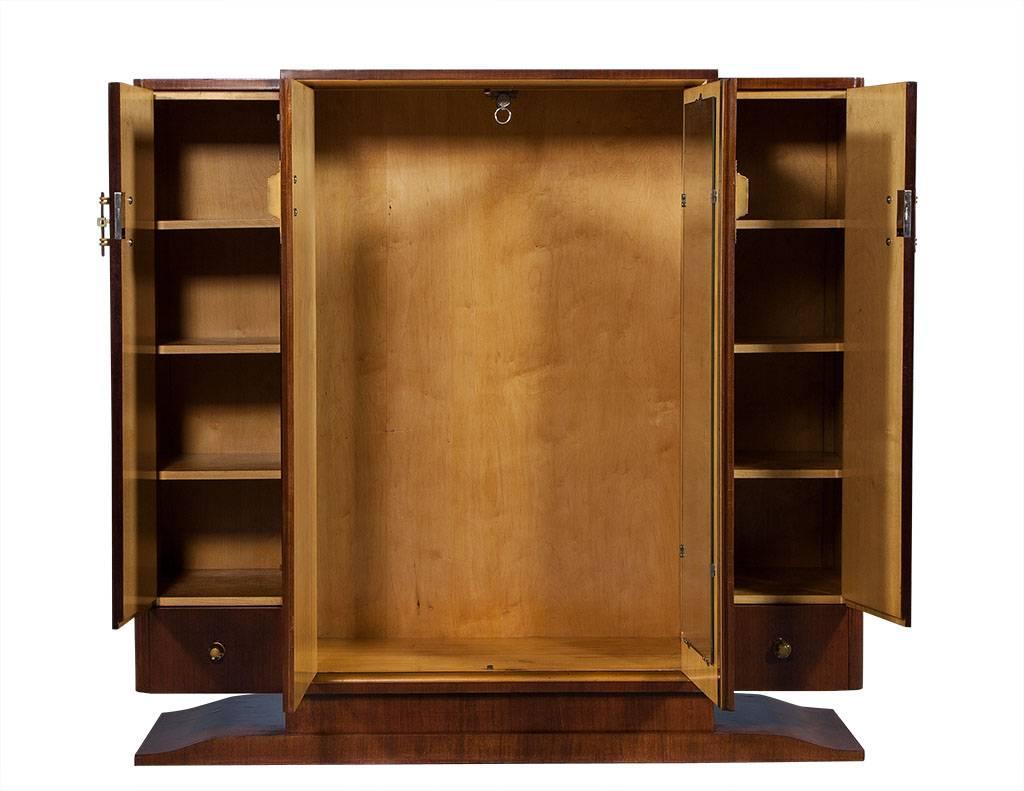 This rosewood armoire divided is into three organizational compartments. Left and right side includes four shelves, as well as two bottom drawers, while middle section includes a clothing rack and full length mirror. Accented acrylic and brass