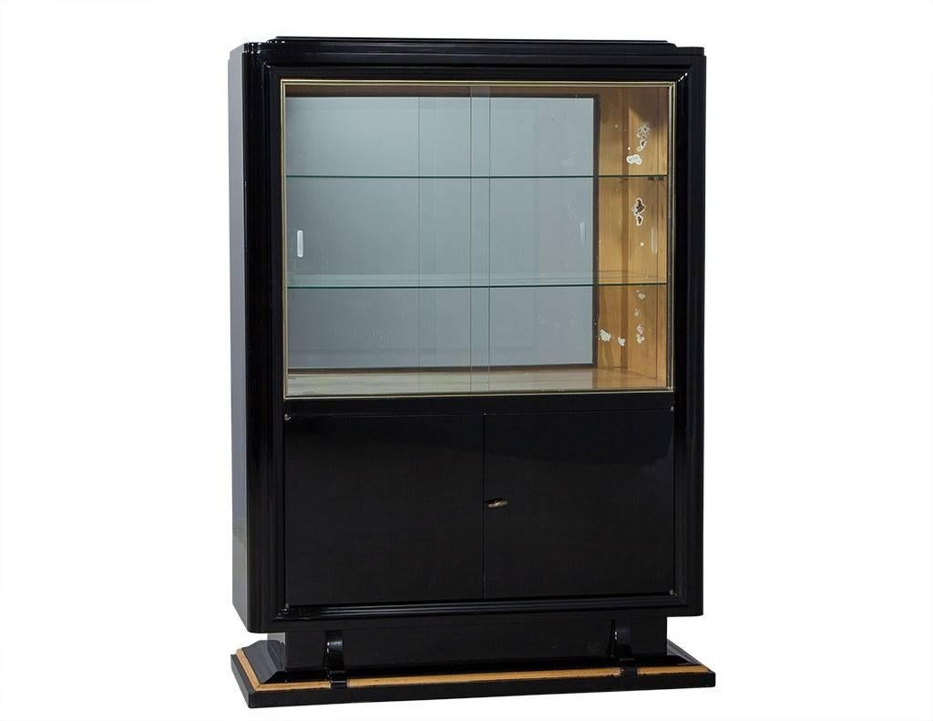 High gloss black cabinet featuring mirrored glass with two glass shelves and sliding glass doors. Bottom has two doors and shelves. Divided into three lower shelved storage compartments, with the upper compartment for display, outfitted with three
