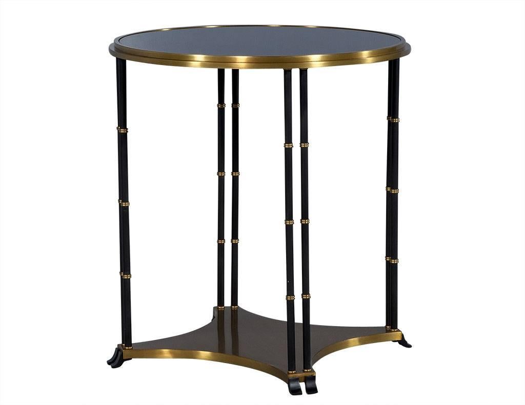 Round black end table is accented with brass banding along both bottom and top parameter. Four double-column legs in the style of bamboo, stem from all brass base and provide support for black glass top. A stand out piece.