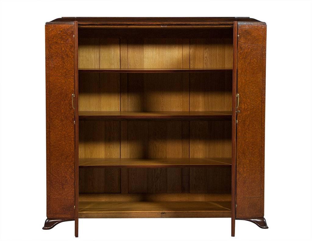 This French Art Deco style armoire is truly elegant. It is crafted out of burled walnut, houses three interior shelves for storage and sits atop four curved feet. It has a sloped top and a decorative diamond-shaped parquetry façade with aged brass