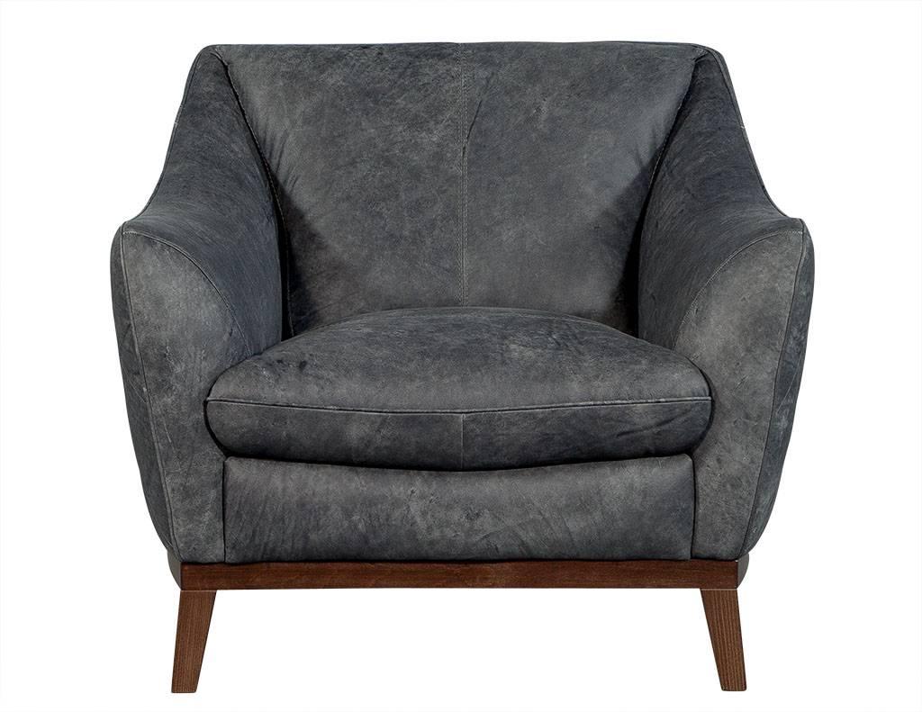These Mid-Century Modern chairs are absolutely luxurious. The distressed, blue-grey leather upholstery sits atop a wooden frame with four feet. The upholstery is adorned with a quilted diamond-shaped pattern along the outside back and the frame is