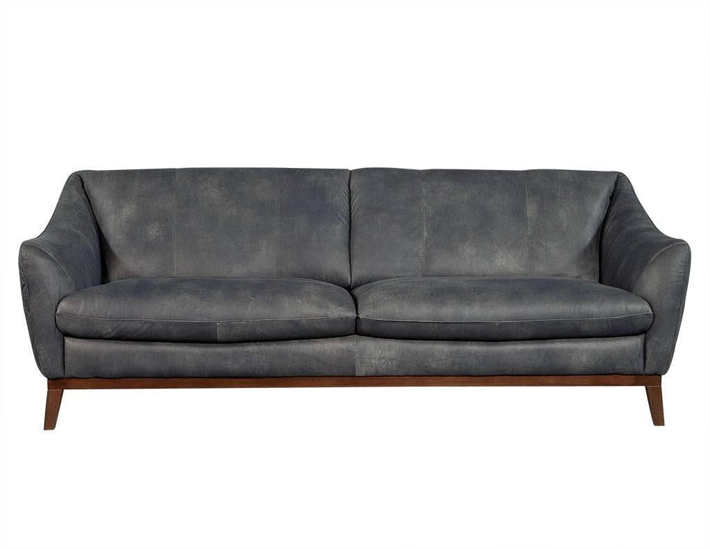 This Mid-Century Modern sofa is absolutely luxurious. The distressed, blue-grey leather upholstery sits atop a wooden frame with four feet. The upholstery is adorned with a quilted diamond-shaped pattern along the outside back and the frame is