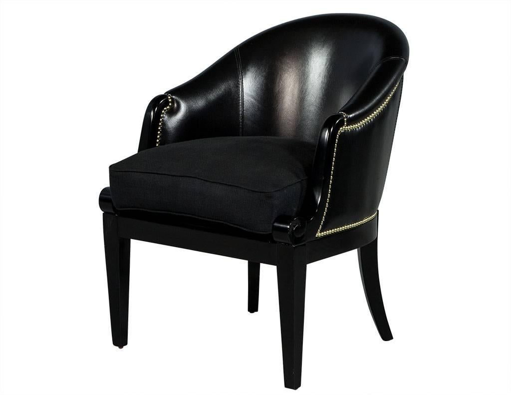 These traditional chairs feature a curved, sloped arm with a black leather chair back adorned with brass nailhead trim along the seams. The semi-detached down-filled seat is upholstered in black linen fabric to add contrasting texture and the show