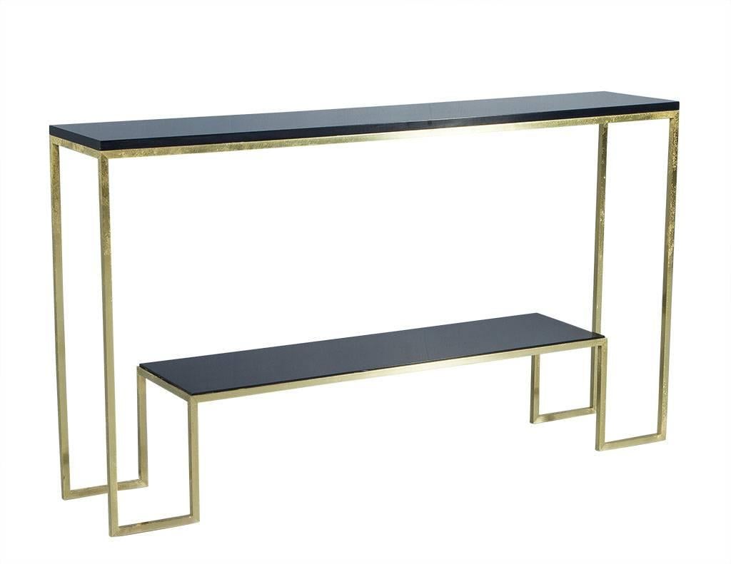 This modern console table is comprised of two tiers with a seamless gold leafed brass frame and black lacquered shelves. Chic and trendy, this piece would complete any entryway or living area.