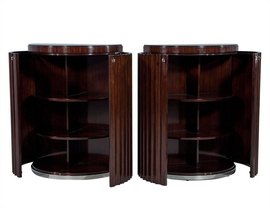 These Art Deco commodes are crafted out of rosewood into a Demilune shape, with louvered double doors with lock and key entry. The interior is divided into two sections, both consisting of three shelves, and the whole piece sits atop a stainless