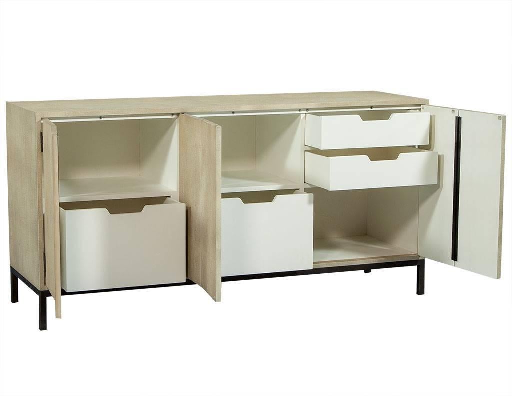 This modern credenza is on trend as can be. It is wrapped in a cream faux shagreen with three push to open doors and a left and middle compartment that includes lower pull-out trays and upper shelving. The right compartment of the piece includes two