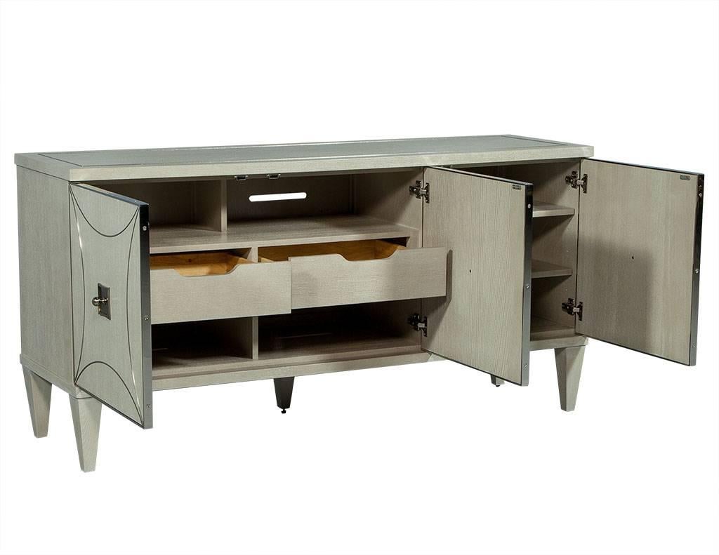 This traditional style media unit is designed by Bernhardt. It is composed of ash solid veneers finished in heather grey with three doors at the front hiding three separate compartments. On the right side are three shelves and inside the left and