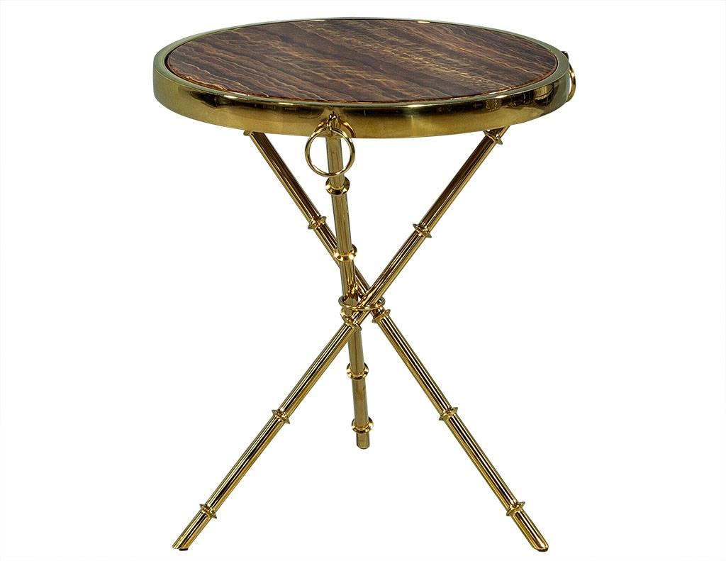 This modern accent table is a mixture of rustic charm and glam luster. It has an inset brown marble top and polished brass frame accented with three decorative rings along the parameter. The piece sits atop three cross legs that add even more of a