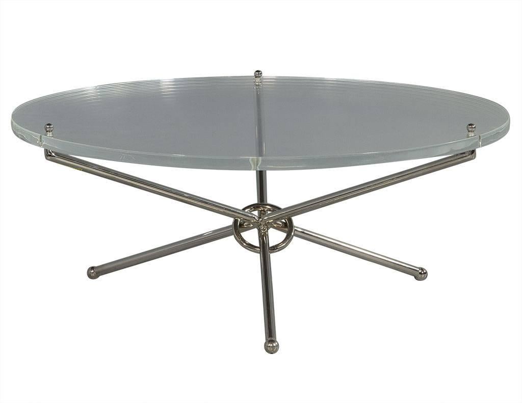 This modern cocktail table is sleek and stylish. It is composed of a thick Lucite top with a polished nickel cross-leg base joined in the centre with a decorative ring. A thought-provoking piece perfect for adding character to any living