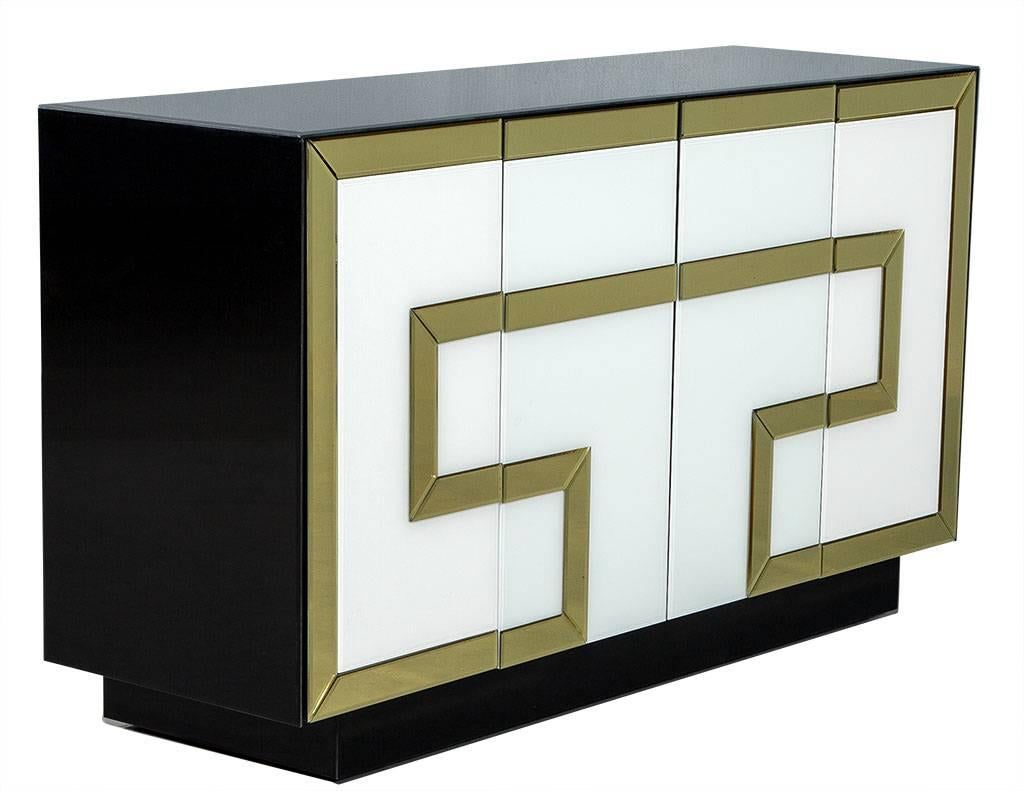 This modern cabinet is composed of a black glass-covered case with opaque glass doors and a gold-mirrored Greek key design. The front has four push to open doors that conceal two storage compartments consisting of two shelves. A perfect addition to