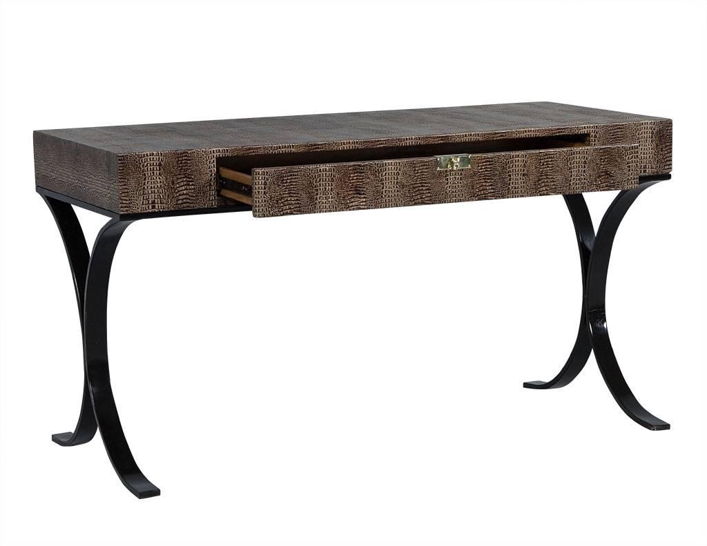 This modern desk is a rich, industrious piece. It contains a single drawer and is wrapped in Hornback crocodile leather. The piece sits atop a tubular, Demilune steel base finished in black and is adorned with a polished brass drawer pull. A perfect