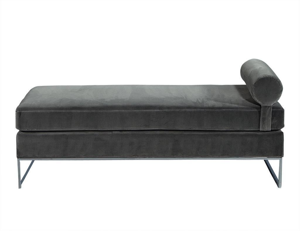 This modern style chaise longue is simply luxurious. It is comprised of a thin, linear polished chrome frame with a detached cushion and removable bolster roll. It is shown upholstered in a commercial grade thick, dove grey velvet but is