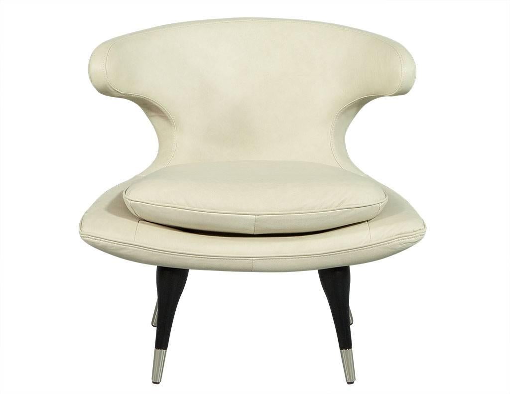 These Mid-Century Modern lounge chairs are classically cool. Upholstered in cream leather, both chairs sit atop four legs finished in matte black with stainless steel caps. The low back has swooping curves along with a removable cushion on a