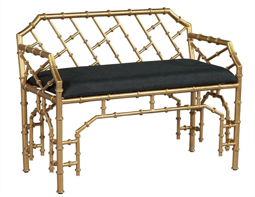 This chinoiserie style gilded bench is a contrast between simplicity and luxury. The gold painted faux bamboo metal frame has a low back and arms with an upholstered woven black fabric seat. Ornate yet comfortable and perfect for a richly designed