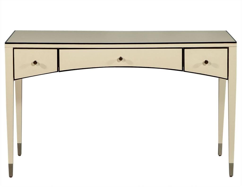 This simple table desk is a functional yet fashionable piece perfect for a small office area. Finished in a cream lacquer accented with black trim, featuring three central drawers with a slight curve that balances out the straight lines of the slim,