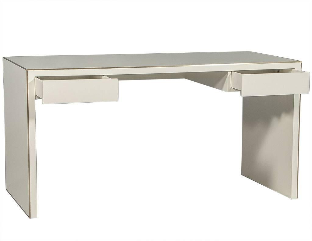 This modern, waterfall style desk is comprised of clean lines and finished in a white lacquer and satin brass trim, there are two drawers on each side that add not only storage but depth to the piece. Perfect for a trendy office.